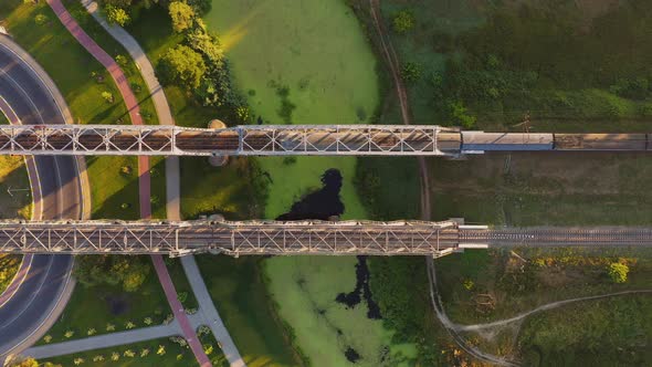 Aerial view of electric train passing the railway bridge across the river from aerial view.