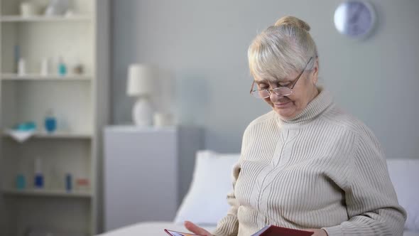 Sad Aged Woman Wearing Eyeglasses and Watching Photo Album, Missing Family