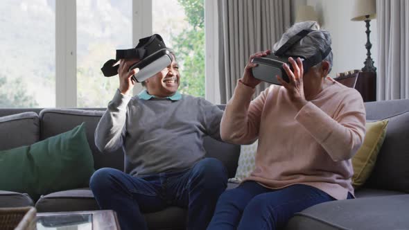 Happy mixed race senior couple wearing vr headset and having fun at home