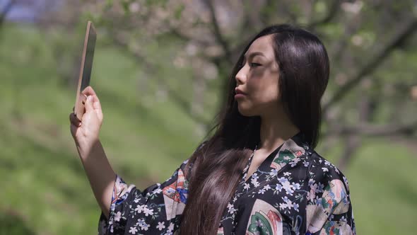 Selfconfident Asian Young Woman in Kimono Looking at Hand Mirror Admiring Reflection