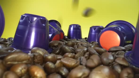 Close up shot of falling roasted coffee beans between coffee capsule in front of yellow background.