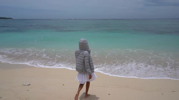 Attractive Young Woman in a Warm Jacket Walking on the Tropical Beach