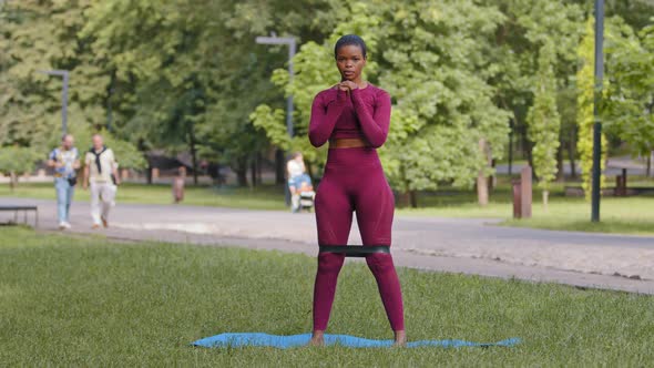 Athletic African Black Girl in Sportswear Exercising Performs Squats with Rubber Band