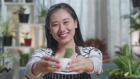 Close Up Of Smiling Asian Woman Holding And Showing Cactus Plant To Camera At Home