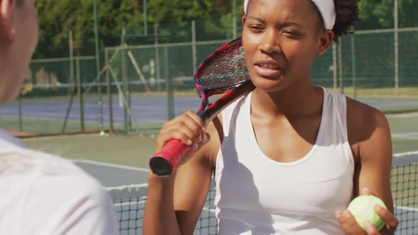 Video of happy african american female tennis player holding racket and talking with friend