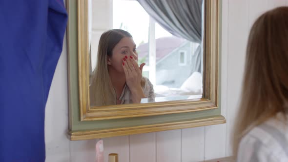 Woman Putting on Concealer before Mirror