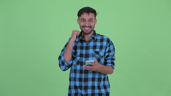 Happy Young Bearded Persian Hipster Man Using Phone and Getting Good News