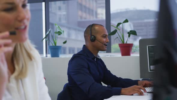 Diverse business people sitting using computers talking with phone headsets