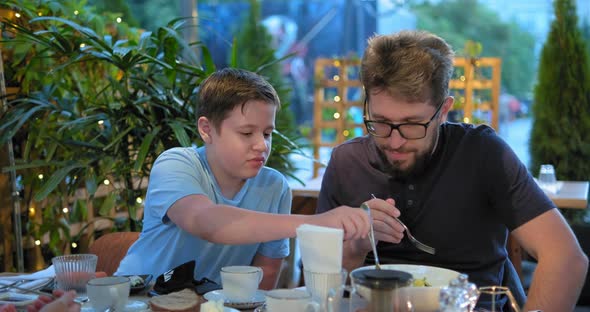 Funny Schoolboy in Blue T-shirt Tries Food of Bearded Dad