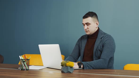 Young Bearded Man Programmer Caucasian Appearance Sitting and Working on a Laptop