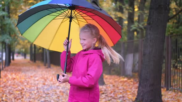 Little Girl Laughing Playing Spinning with Rainbow Umbrella Autumn on Fallen Golden Orange Maple