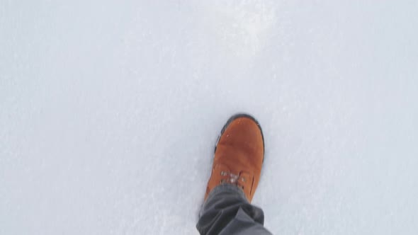 Feet of a man walking on loose snow with a view from above.