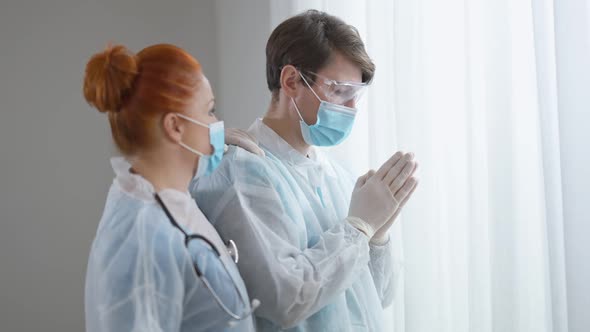 Side View of Empathic Nurse Supporting Doctor Praying Indoors