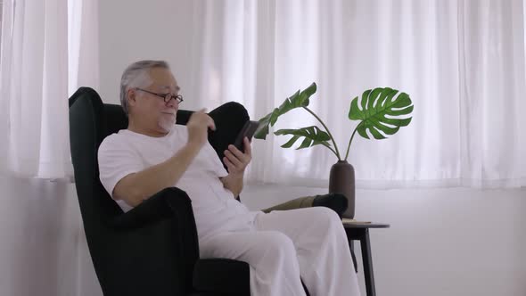 Asian Elderly man use smart phone in living room on a relaxing day.