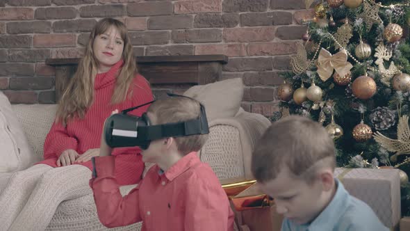 Mother Sitting on Sofa Watches Sons Playing with Gifts