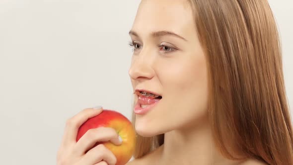 Blonde Girl with Braces Eating Apple. White. Closeup