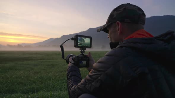 Man Adjusting Camera With Monitor In Dawn Landscape