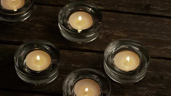 Tea candles with flaming wicks on a wooden background - CANDLES 001