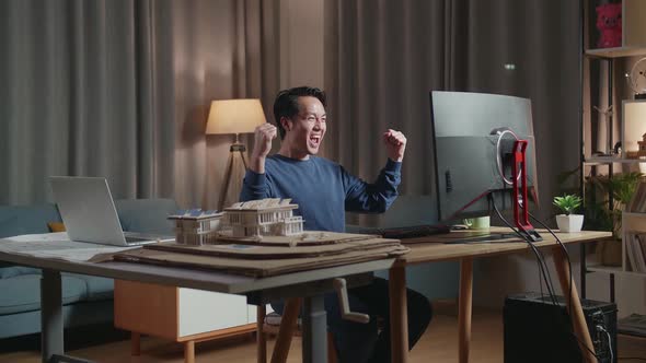 Asian Male Engineer With The House Model Celebrating While Working On A Desktop At Home