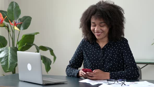 African American Attractive Smart Successful Positive Woman Sits in Modern Office Uses Smartphone