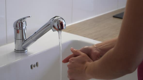 Woman washing her hands in the kitchen sink.