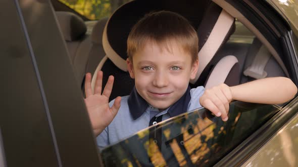 A Boy is Wearing a Seat Belt in a Child Seat in the Car He Waves His Hand