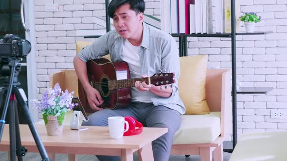 Asian man is playing the guitar and singing on social media by streaming live from his home.