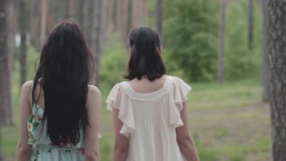 Back of Two Beautiful Women with Long Hair in Short Dresses Walking in the Forest with Basket