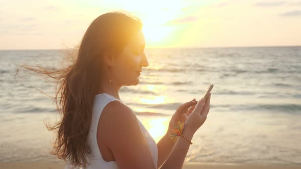 Smiling Girl Uses Smartphone on Beach at Tropical Resort