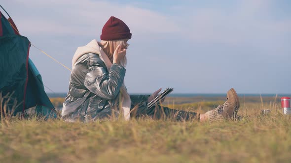 Blonde Lady in Jacket with Tablet at Tent on Dry Grass