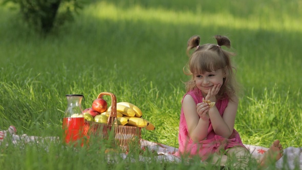 Weekend at Picnic. Caucasian Child Girl on Grass Meadow with Basket Full of Fruits. Eating Pancakes