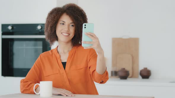 African Millennial Woman with Curly Hair Girl in Orange Blouse Female Vlogger in Kitchen at Home