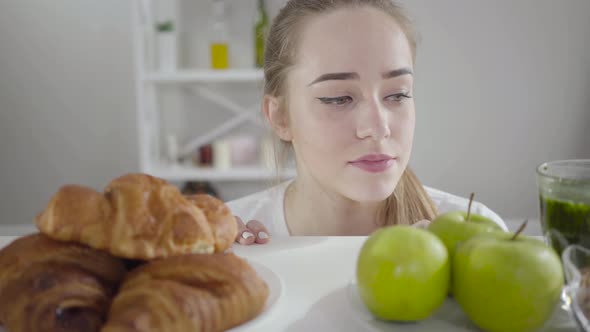 Portrait of Beautiful Slim Girl Choosing Between Green Apples and Crusty Croissants