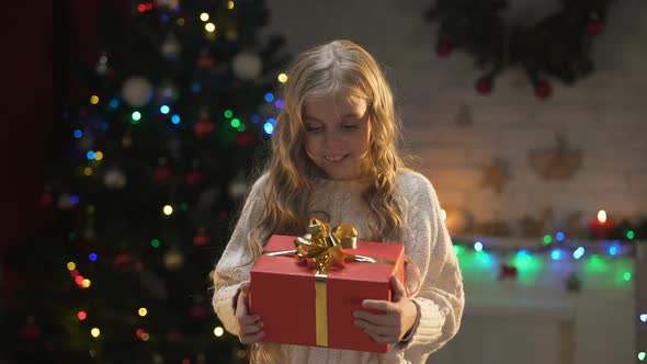 Cute Little Girl Hugging Christmas Present Near Sparkling Decorations, Dreams