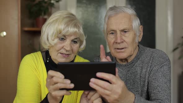 Pretty Mature Senior Couple Grandparents Enjoy Online Shopping on Tablet at Home