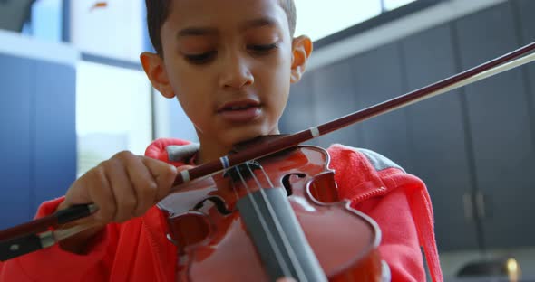 Front view of attentive Asian schoolboy playing violin in classroom at school 4k