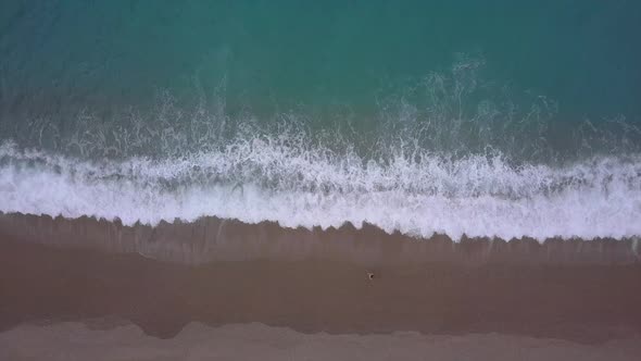 Aerial top view turquoise waves break on empty pebble beach. Pure calm sea from bird's eye view