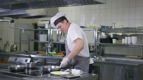 Portrait of Male Cook in Uniform Cleaning Kitchenware in Restaurant Kitchen Indoors