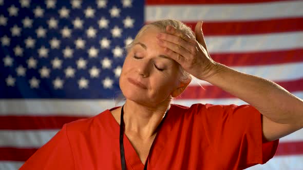 Medium tight portrait of nurse looking very worried and sad rubbing her forehead with American flag