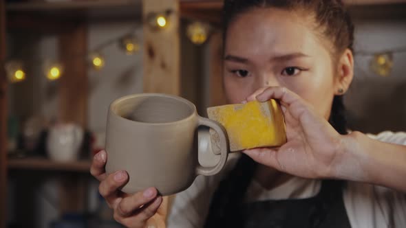 Young Woman Potter Smoothing the Surface of Cup Handle Using a Sponge