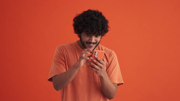 Laughing curly-haired Indian man looking at the phone