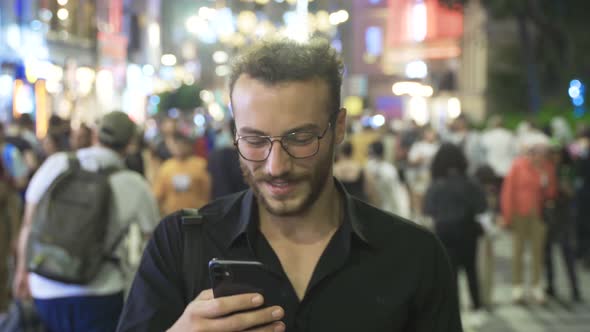 Young man using phone in night crowd.