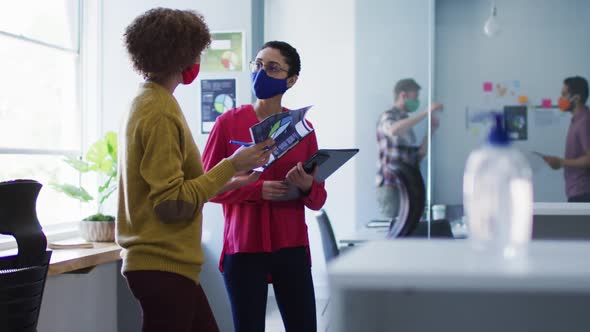 Mixed race female colleagues wearing face masks in office