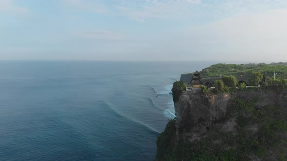 Aerial orbit shot around a Temple located near high rough cliffs and surrounded with ocean in Bali