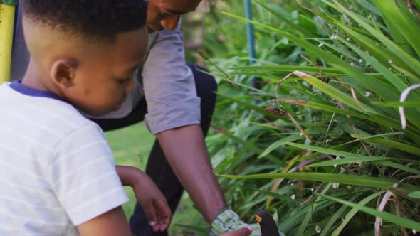 Happy african american father and son, taking care of plants outdoors