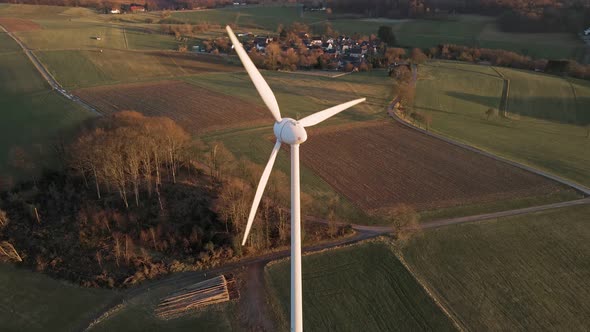 Aerial footage of a large, white wind turbine in North Rhine Westphalia, Germany during a sunset in