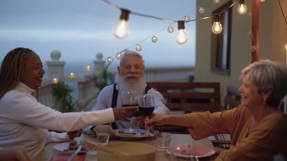 Happy multiracial seniors toasting with red wine glasses together on house patio dinner