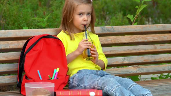 Girl Sits in Schoolyard and Drinks Juice