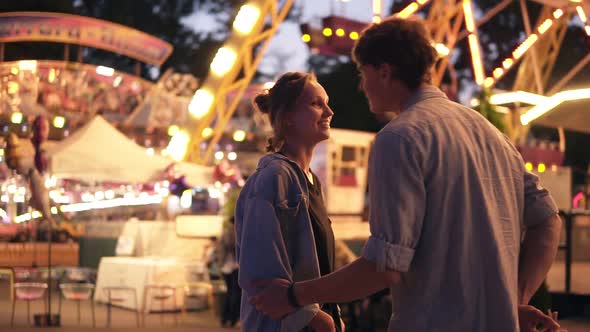 Side Portrait of an Attractive Young Couple Meeting in an Amusement Park with a Colorful Brightful