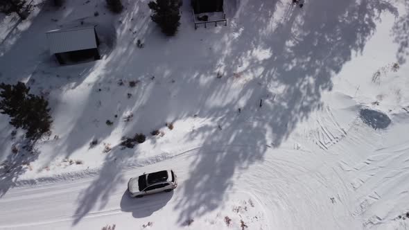 Family leaving mountain cabin on snow covered backcountry road during the day, top down aerial
